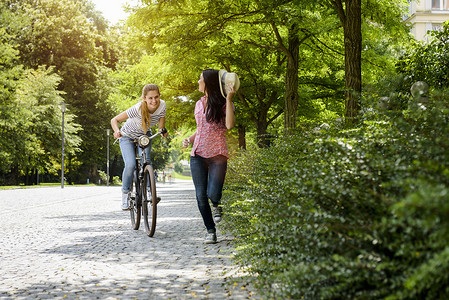 骑着自行车微笑的年轻女子追赶戴着巴拿马帽子的年轻女子的前景