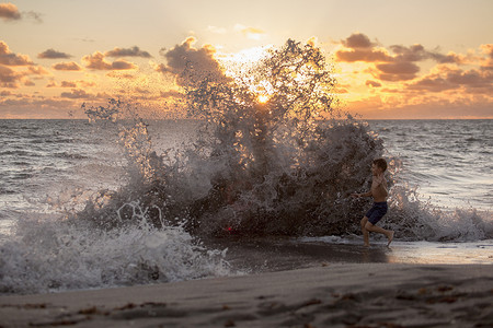 美国佛罗里达州朱庇特岛男孩在日出时在溅起的海浪中玩耍吹石保护区