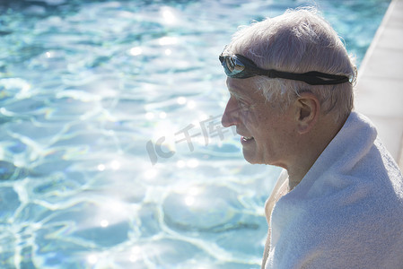 坐在室外游泳池边的老年男子毛巾披在肩膀上