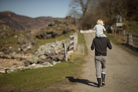 小路摄影照片_父亲将儿子扛在肩上走在小路上后视