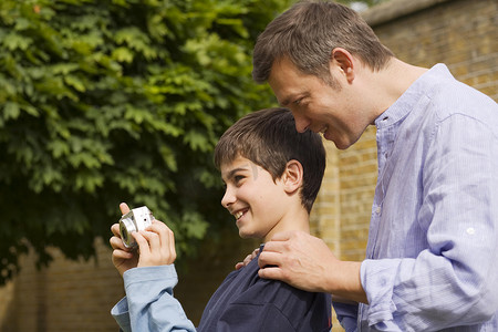 成熟男子在花园里向儿子解释数码相机