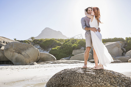 海滩婚礼摄影照片_一对夫妇站在岩石上拥抱的全景