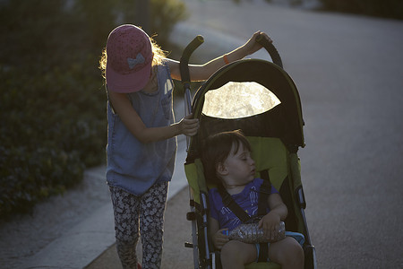 日落时分一个女孩推着推着婴儿车的妹妹穿过公园