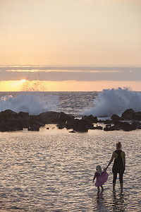 儿童培育摄影照片_美国夏威夷科纳轮廓分明的蹒跚学步的女孩子和母亲在海里划桨看着海浪溅起的浪花