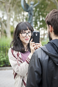 年轻女子在公园里用智能手机给男朋友拍照的背影