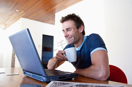 男士一边喝咖啡一边使用笔记本电脑