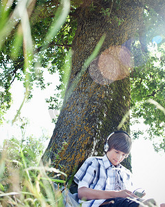 镜头焦距摄影照片_戴耳机的男孩靠在树上