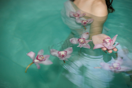 年轻女子在水疗游泳池里漂浮的紫色兰花的剪裁照片