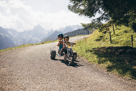 骑男孩摄影照片_戴着头盔的母子在弯道上骑着卡丁车张开相机嘴奥地利弗拉尔贝格布卢登茨