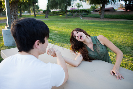 一对年轻夫妇在公园的野餐长凳上假装摔跤