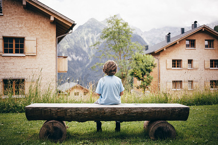 男孩坐在圆木长凳上望向远处山景的后景