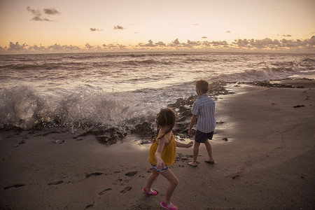 美国佛罗里达州朱庇特岛男孩和妹妹在黎明时分逃离海滩上溅起的海浪吹石保护区