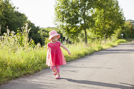 向阳而行摄影照片_蹒跚学步的女孩子看着她的影子沿着乡村道路蹒跚而行