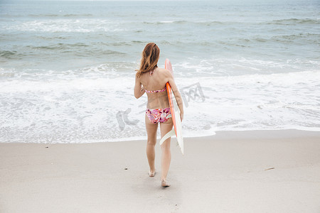 中年女性运动摄影照片_中年妇女走向大海手持冲浪板后视