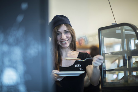 职场用具摄影照片_咖啡馆里拿着盘子和蛋糕片的年轻女服务员的肖像
