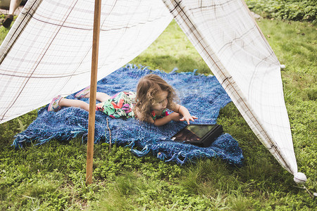 躺在自制花园帐篷里的女孩使用数字平板电脑上的触摸屏