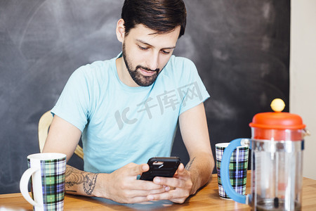 年轻人坐在桌子旁喝着咖啡看着智能手机