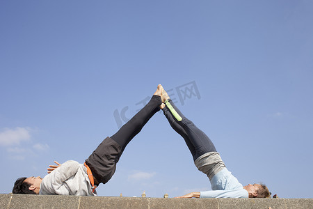 墙纸蓝摄影照片_在蓝天下练习杂技瑜伽的男人和女人
