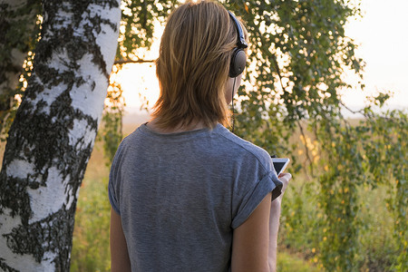 女人戴着耳机从林地向外看的背影