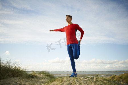 一名男子在沙丘上单腿站立做伸展运动