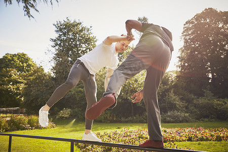 一名男子与私人教练手牵手在公园栅栏上单腿保持平衡