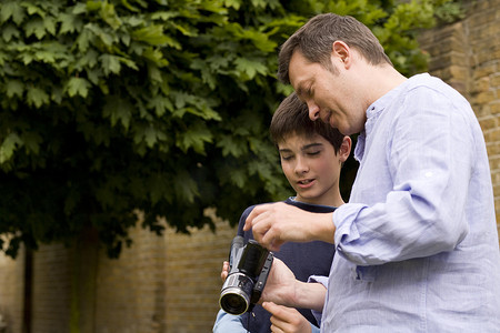 成熟男子在花园里向儿子解释摄像机