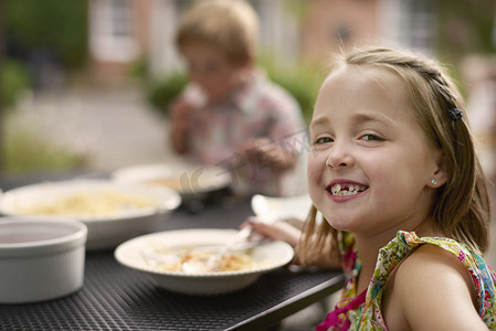 女孩在花园里的餐桌旁用餐望着镜头微笑