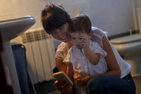 中年妇女和女婴低头看着浴室里的智能手机