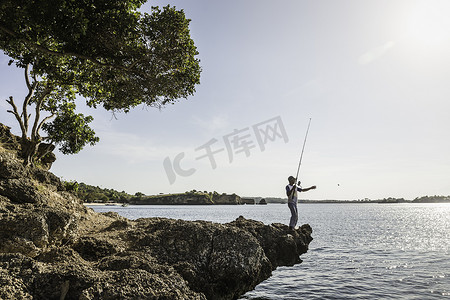 印度尼西亚龙目岛粉色海滩上的男人在岩石上钓鱼