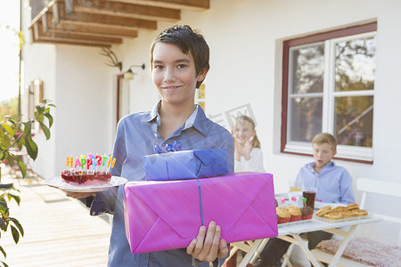 十几岁的男孩在露台上拿着生日蛋糕和生日礼物的肖像
