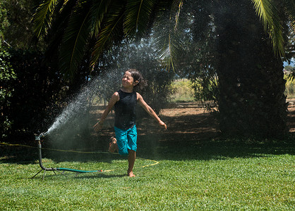 从花园洒水器里跑过水的男孩
