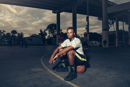 篮球场上的一名男子坐在篮球上看着摄像机