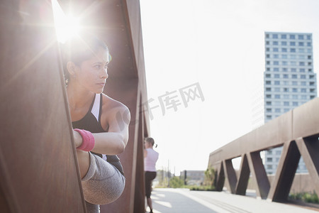 女子在阳光普照的城市人行桥上抬腿训练