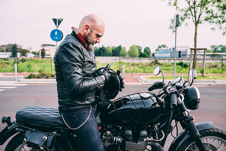 成熟的男性摩托车手坐在摩托车上检查头盔