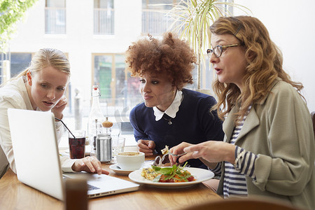 街边警示摄影照片_三位女性朋友在咖啡馆边吃午饭边看笔记本电脑