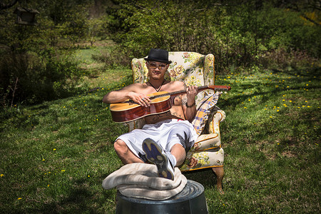 一名男子坐在花园的扶手椅上弹吉他