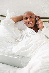 躺在床上的男人拿着笔记本电脑和手机