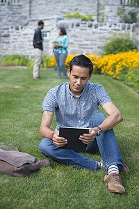 凯格尔摄影照片_坐在草地上的男学生使用数字平板电脑