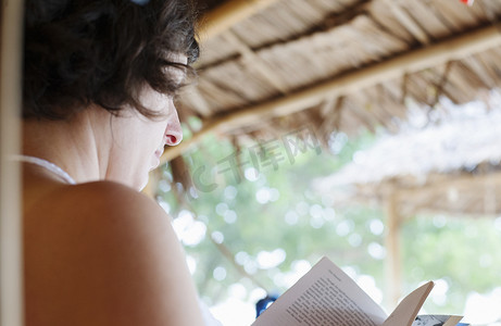 东南亚人摄影照片_在泰国克拉丹的海滩小屋外看书的女人的肩膀上