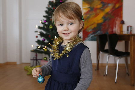 圣诞树前的女孩戴着金属饰品拿着小玩意儿看着镜头微笑