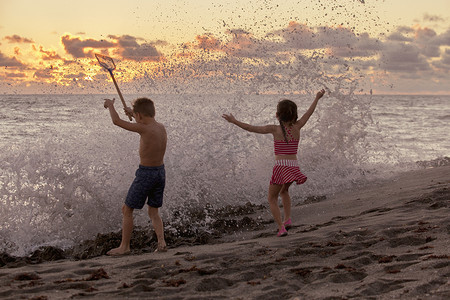 日出时男孩和妹妹在溅起的海浪中玩耍的后景美国佛罗里达州朱庇特岛吹石保护区