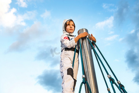 宇航员服装摄影照片_穿着宇航员服装的男孩从攀登架的顶部向外看