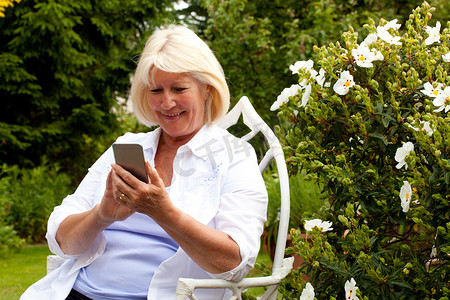 老女性摄影照片_坐在花园里看智能手机的老妇人