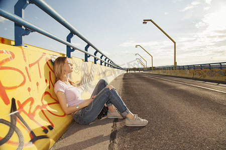 阳光下一名年轻女子靠在桥上的涂鸦墙上坐着