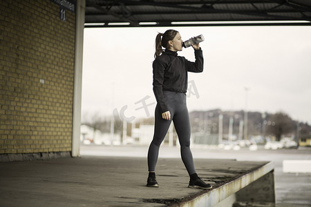机械转轮摄影照片_在仓库平台上喝瓶装水的女跑步者