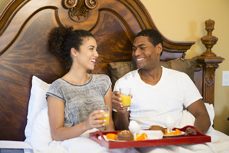 橙汁海报免费摄影照片_一对夫妇坐在床上面对面地笑着吃早餐