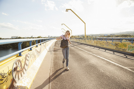 在桥上走摄影照片_走在桥上的年轻女子看着肩包