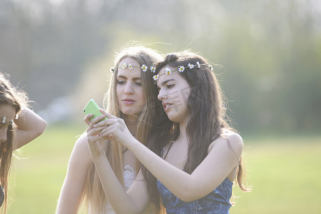两名十几岁的女孩戴着雏菊链条头巾在公园里阅读智能手机短信