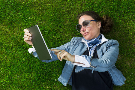 在数字平板电脑上使用触摸屏俯瞰躺在草地上的成熟女性