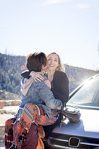光斑玻璃摄影照片_汽车引擎盖上的年轻情侣拥抱亲吻脸颊微笑美国洛杉矶加利福尼亚州奇劳露营地
